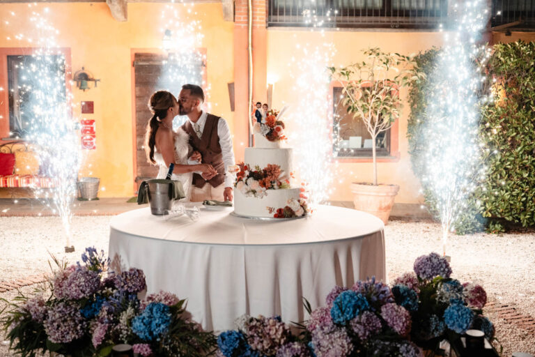 Wedding cake on a round table banked with blue hydrangeas, with sparkle fountains behind, Letizia T. Events