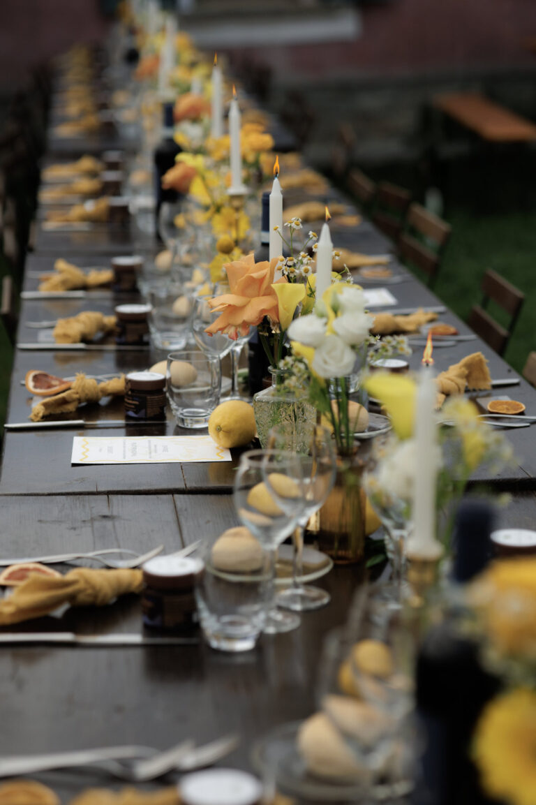 Long dark table set with candles, yellow flowers and napkins for a dinner outdoors, Letizia T. Events