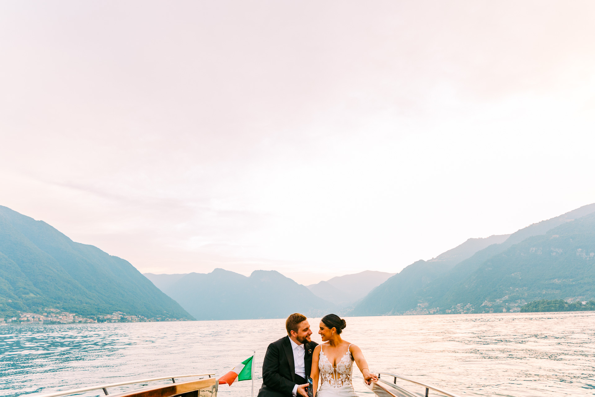 Victoria and Ryan on a boat heading out across Lake Como at dusk, the mountains folding away behind them, Light & Dreams
