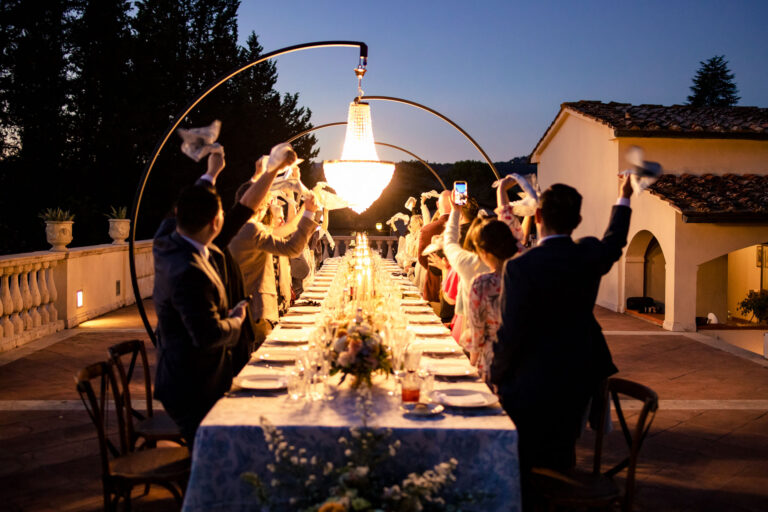 Guests raising napkins at the long dinner table on the terrace at Villa La Selva, Tuscany, Light & Dreams