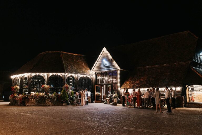 The forecourt at night, with the lit Engine House and the gabled entrance of the Great Barn, Lillibrooke Manor