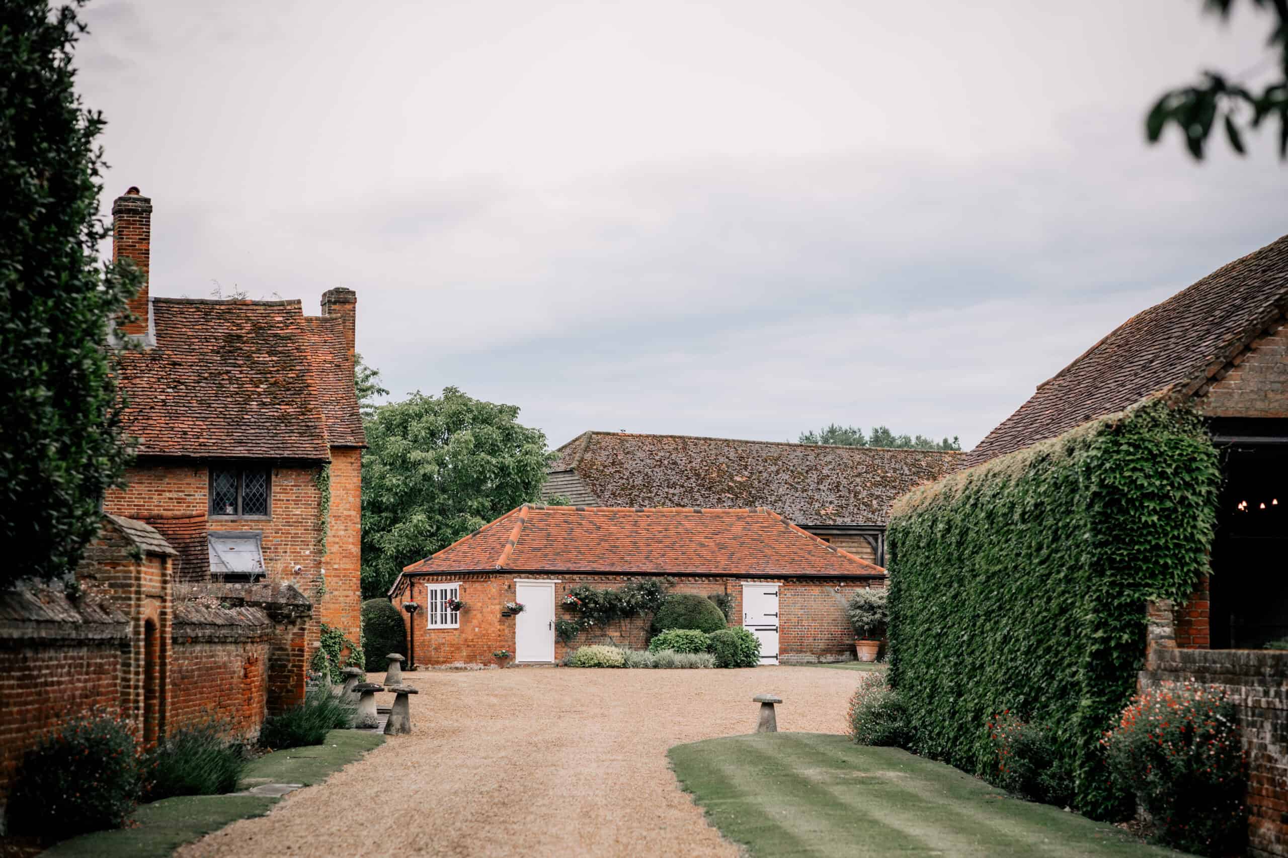 The gravel drive between the red-brick Manor House, a low brick outbuilding and an ivy-covered barn wall, Lillibrooke Manor