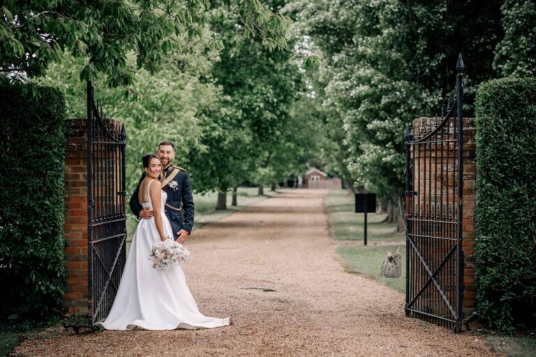 A couple at the wrought-iron gates, with a tree-lined avenue running away behind them, Lillibrooke Manor