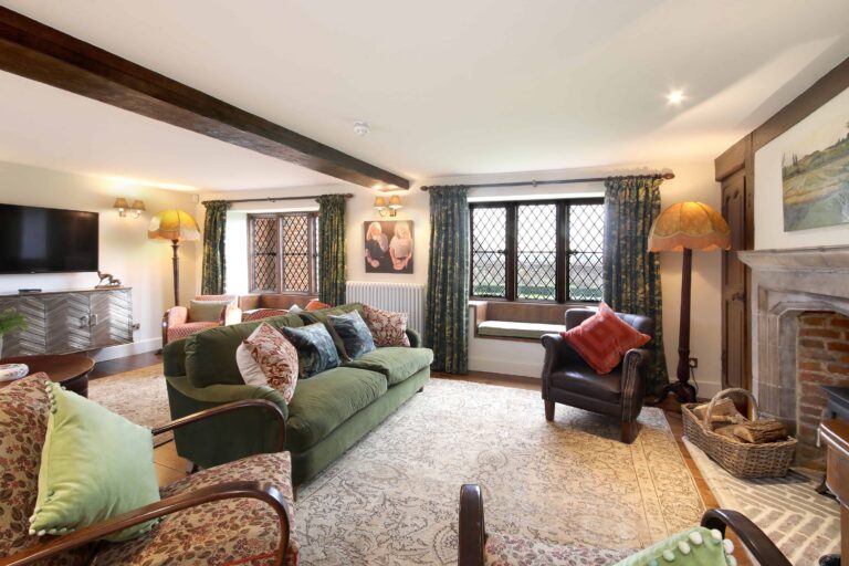 The Manor House sitting room, with leaded windows, a stone fireplace and sofas, Lillibrooke Manor