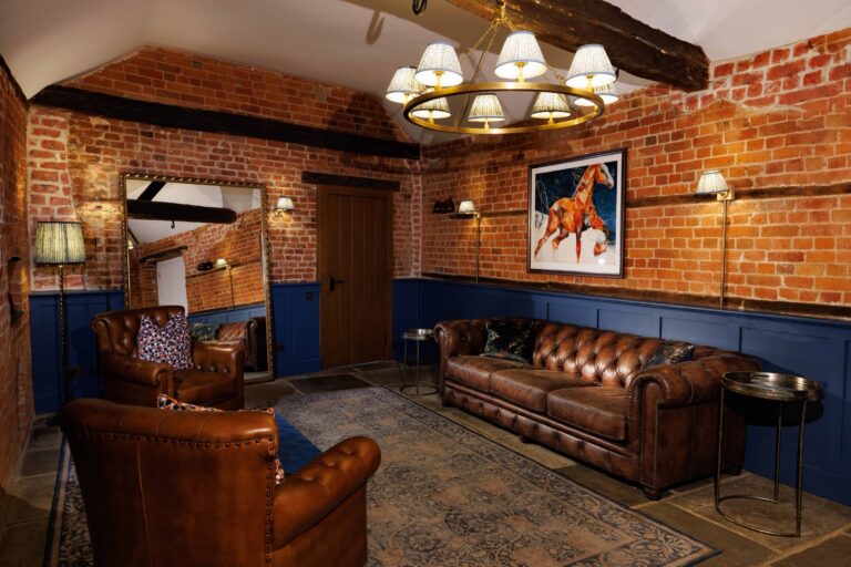 A preparation room with exposed brick, Chesterfield sofas and armchairs and a brass chandelier, Lillibrooke Manor