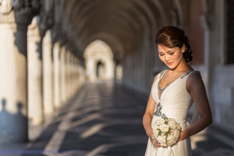 A bride in the arched colonnade at the Doge's Palace, holding white roses, Lisa Semenzato