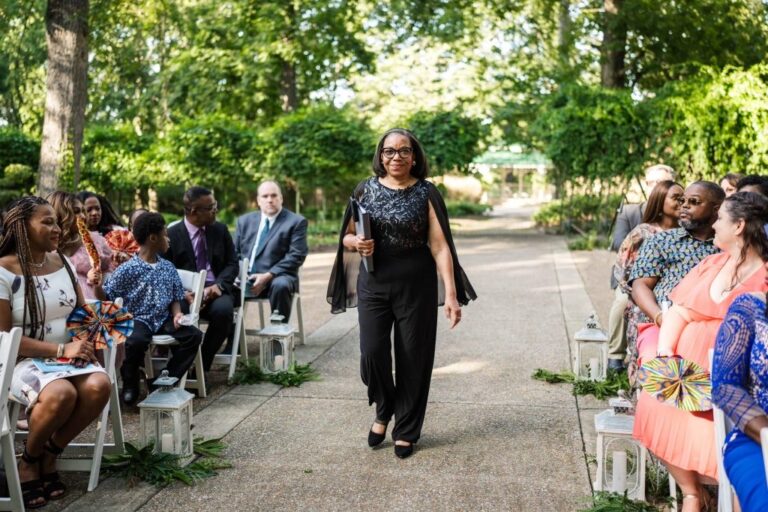 The officiant walks the garden path between rows of seated guests at the start of a ceremony, Living Ceremonies