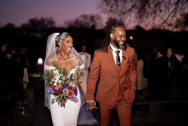 A couple walking at dusk, the bride carrying a colourful bouquet, Living Ceremonies