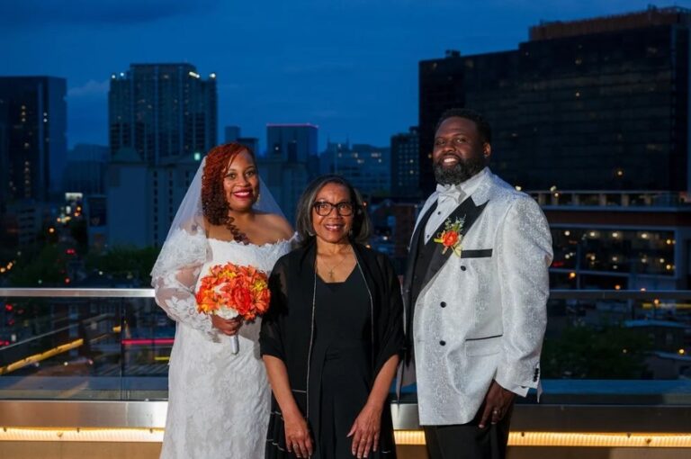 A couple with their officiant on a rooftop with the city lit up at dusk, Living Ceremonies