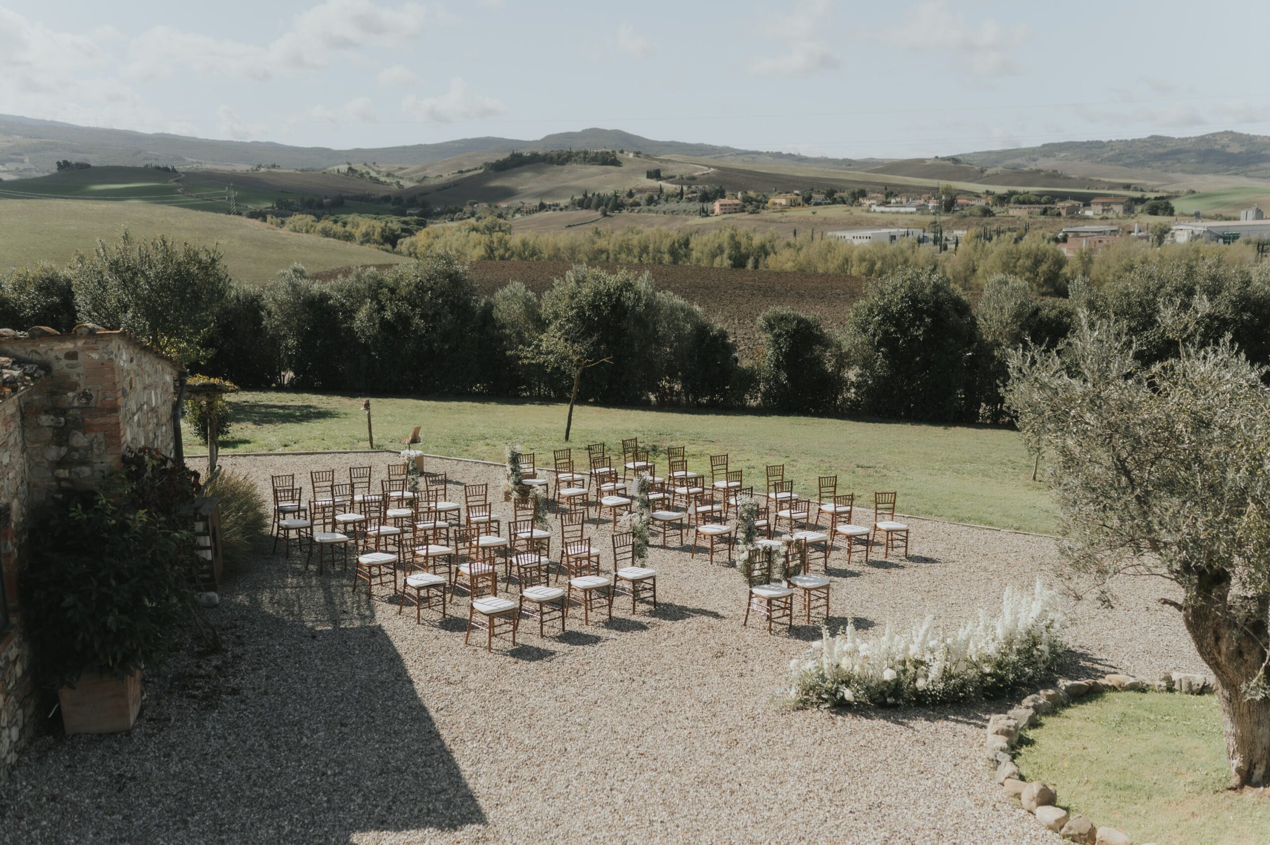 Rows of wooden chairs set for a ceremony on the lawn terrace, the hills of the Val d'Orcia behind, Locanda in Tuscany