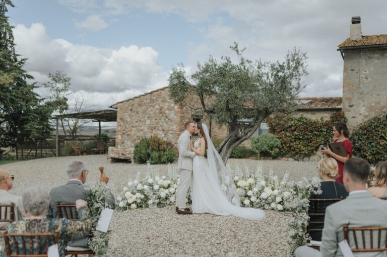 A couple embracing at a ceremony beside an olive tree and the stone building, Locanda in Tuscany