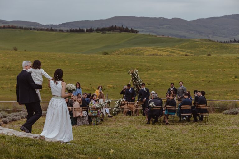 A small outdoor ceremony in the open field, guests seated on the grass, Locanda in Tuscany