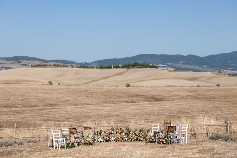 Chairs and a flower arrangement set for a ceremony in the dry wheat field, Locanda in Tuscany