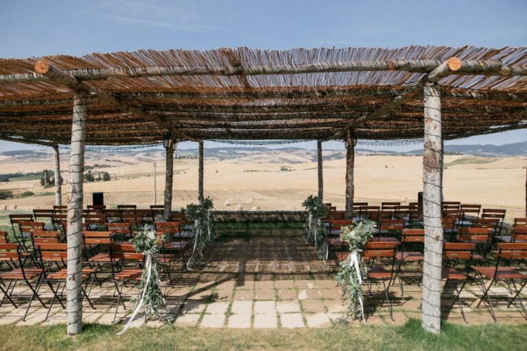 Wooden chairs set for a ceremony beneath the reed-roofed pergola, Locanda in Tuscany