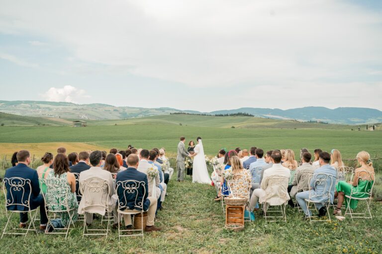 Guests seated on chairs in a green field for an outdoor ceremony, Locanda in Tuscany