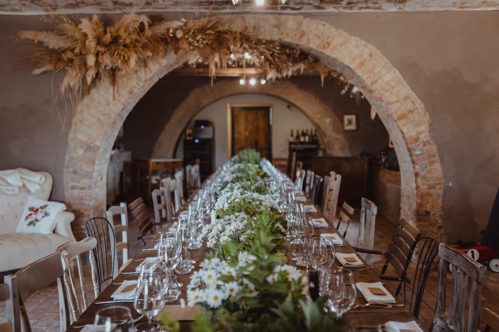 A long table set for dinner beneath the stone arch, Locanda in Tuscany