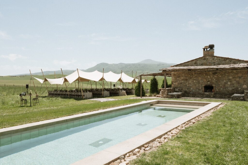The swimming pool beside the stone farmhouse, with a tent set up on the lawn beyond, Locanda in Tuscany