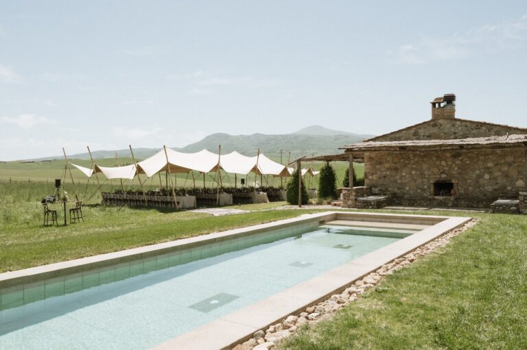 The swimming pool beside the stone farmhouse, with a tent set up on the lawn beyond, Locanda in Tuscany