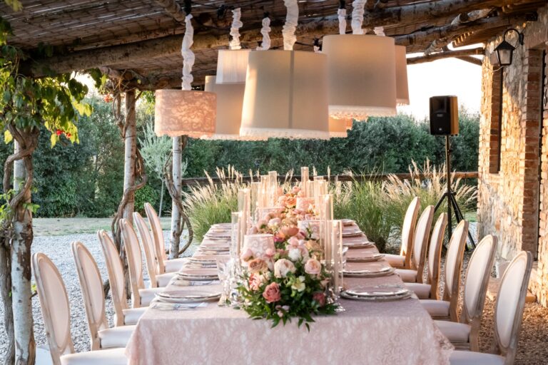 A long table set for dinner beneath the pergola, with hanging lamp shades, Locanda in Tuscany