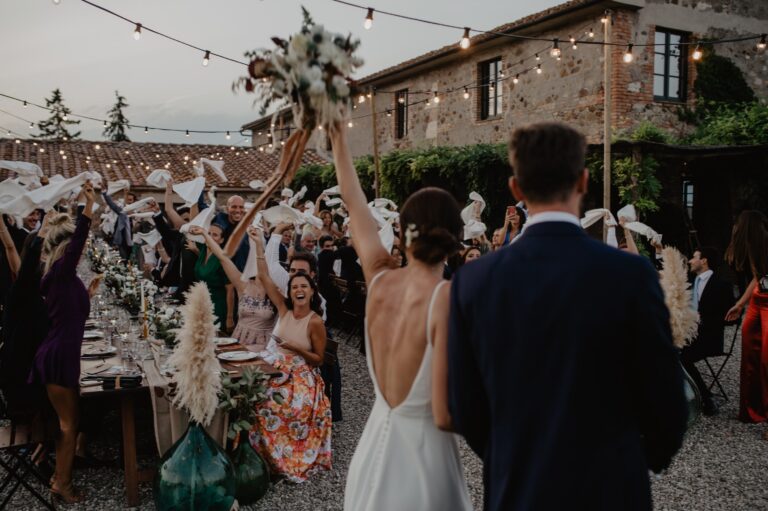 The couple with their arms raised as guests cheer at a dinner in the courtyard, Locanda in Tuscany