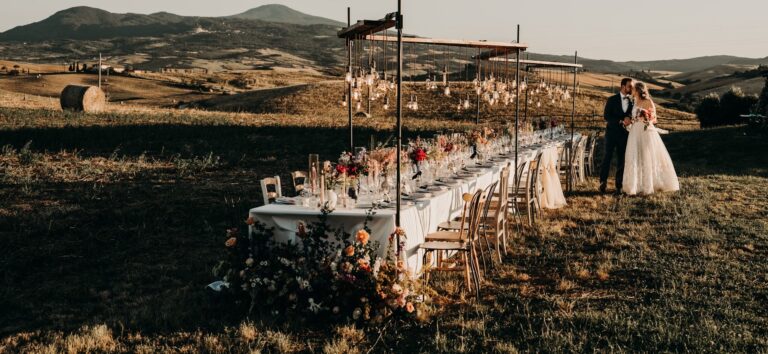 A long table set in the fields at sunset, the couple beside it, Locanda in Tuscany