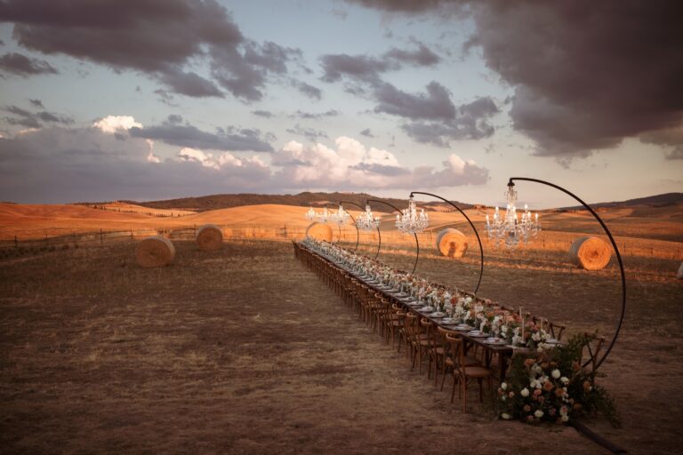 A long table with chandeliers on curved stands in a field at sunset, Locanda in Tuscany