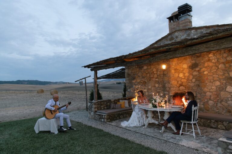 A guitarist playing beside a table by the stone building at dusk, Locanda in Tuscany