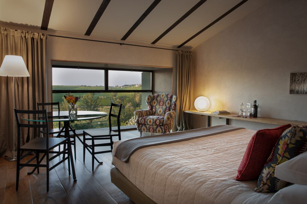 A bedroom with a window looking over the hills, a bed and a small table, Locanda La Raia