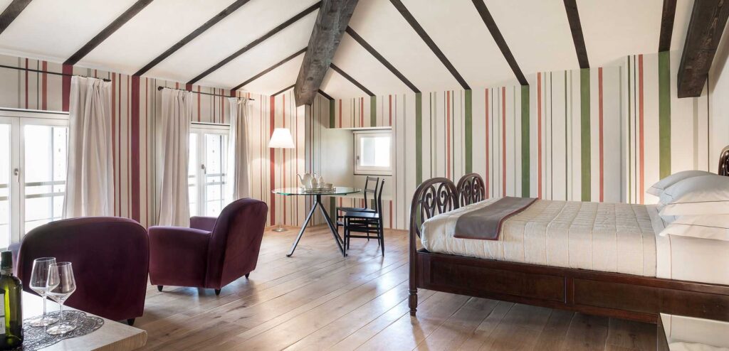 A bedroom with striped curtains, a double bed and two armchairs, Locanda La Raia