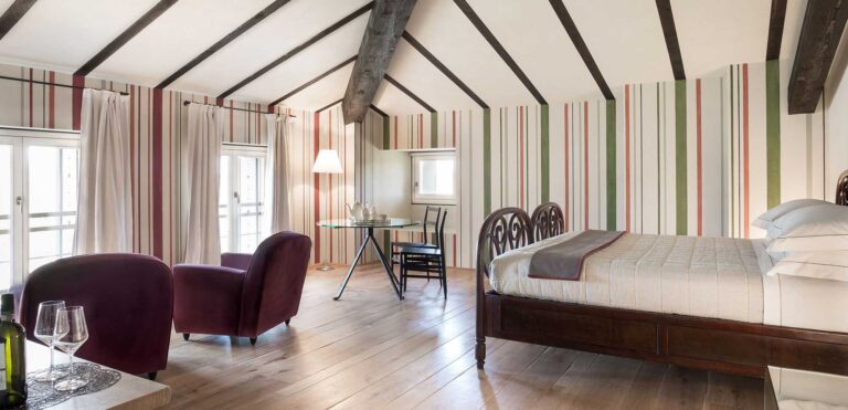 A bedroom with striped curtains, a double bed and two armchairs, Locanda La Raia