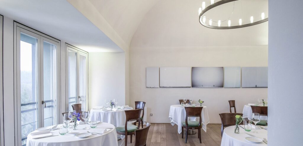 The restaurant, with round tables set beside tall windows, Locanda La Raia