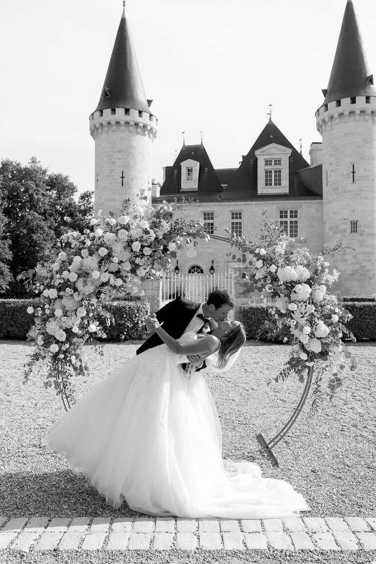 An embrace beneath a floral arch at the château, Lorella Giannini