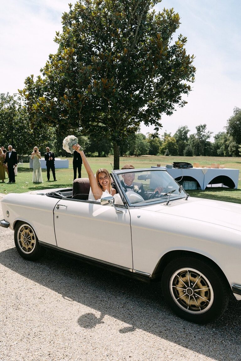 A bride waves from a vintage convertible, château behind, Lorella Giannini