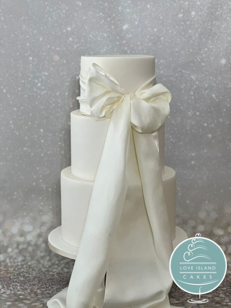 A three-tier white cake finished with a large sugar bow, Love Island Cakes