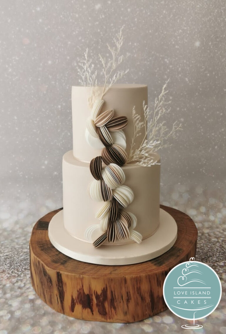 A two-tier cake with sculpted ribbon detail and dried grasses on a wooden base, Love Island Cakes
