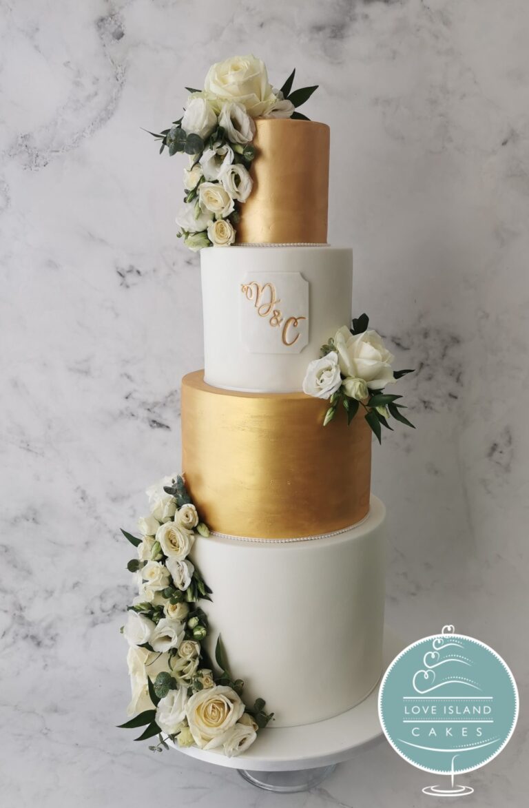 A four-tier cake with white and gold leaf tiers and a trailing floral cascade, Love Island Cakes