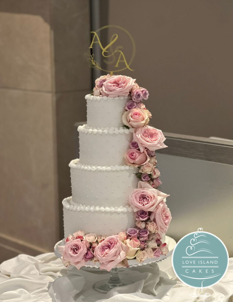 A four-tier white cake with a cascade of pink and blush roses and a gold monogram topper, Love Island Cakes
