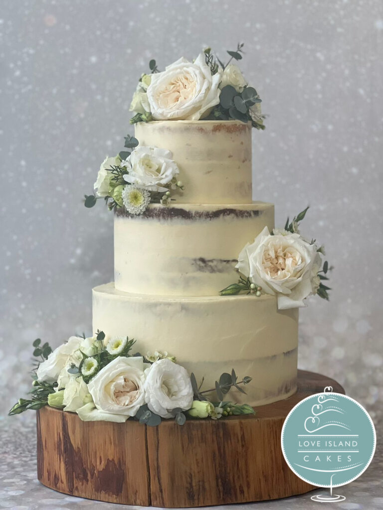 A three-tier semi-naked cake with ivory garden roses on a wooden slice, Love Island Cakes