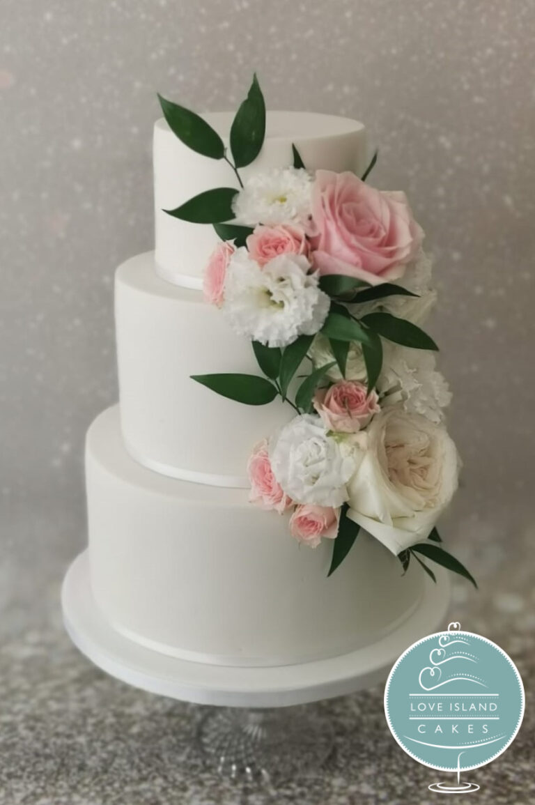 A smooth white three-tier cake with a cascade of pink roses, white blooms and greenery, Love Island Cakes