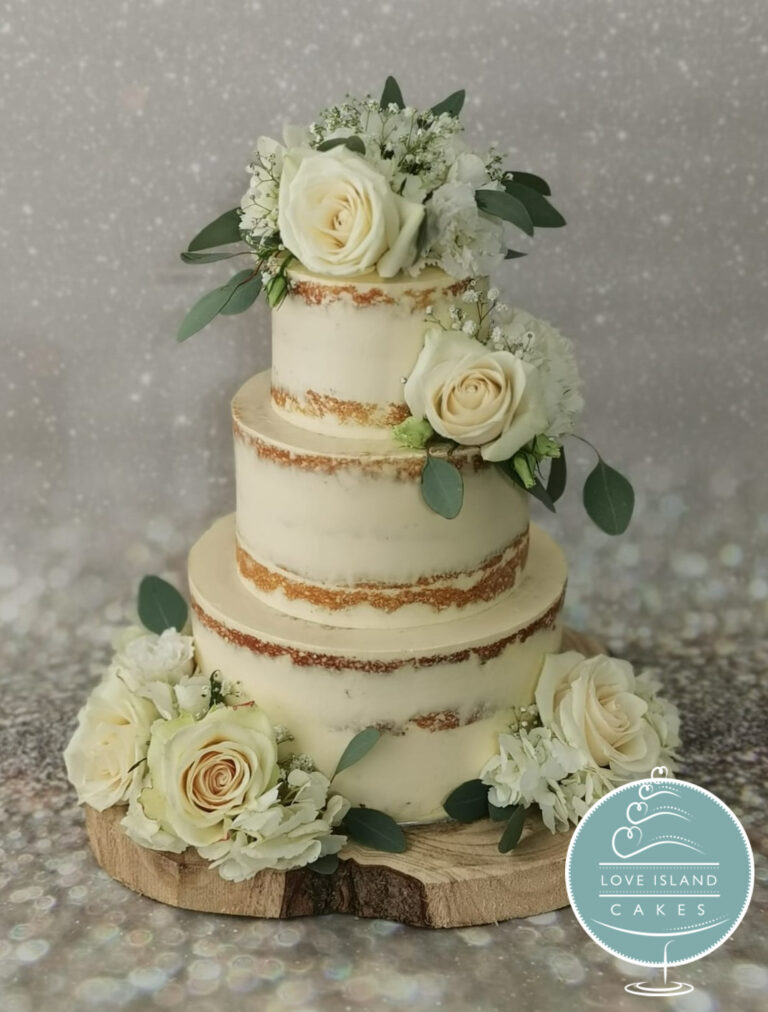 A four-tier semi-naked cake with white roses and greenery on a wooden slice, Love Island Cakes