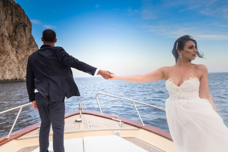 The couple holding hands on the bow of a boat beneath Capri's cliffs; styled wedding shoot, Lovexposed Photography