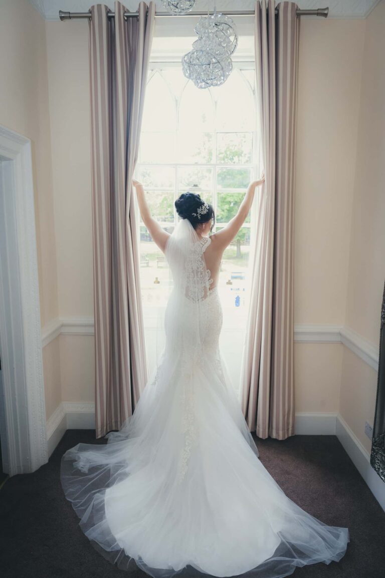 The bride in her gown against the window light; Joelle and Tashan's wedding at Gilwell, Essex, Lovexposed Photography