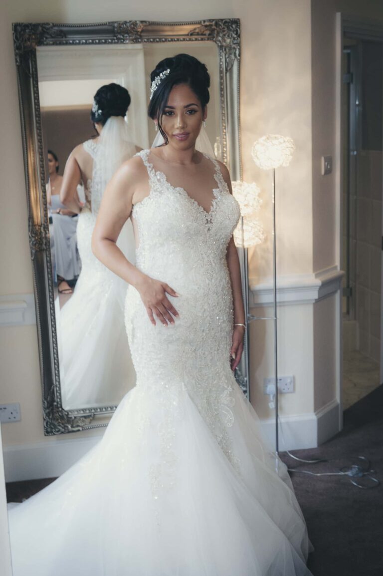 The bride checks her dress in the mirror; Joelle and Tashan's wedding at Gilwell, Essex, Lovexposed Photography