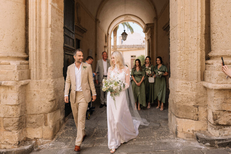 Emily and Richard leave the ceremony through a stone archway in Noto, LOVIÙ Events