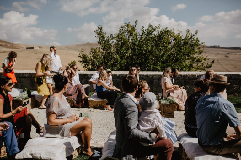 Guests seated outdoors for a ceremony at Masseria Susafa, with the inland hills behind, LOVIÙ Events