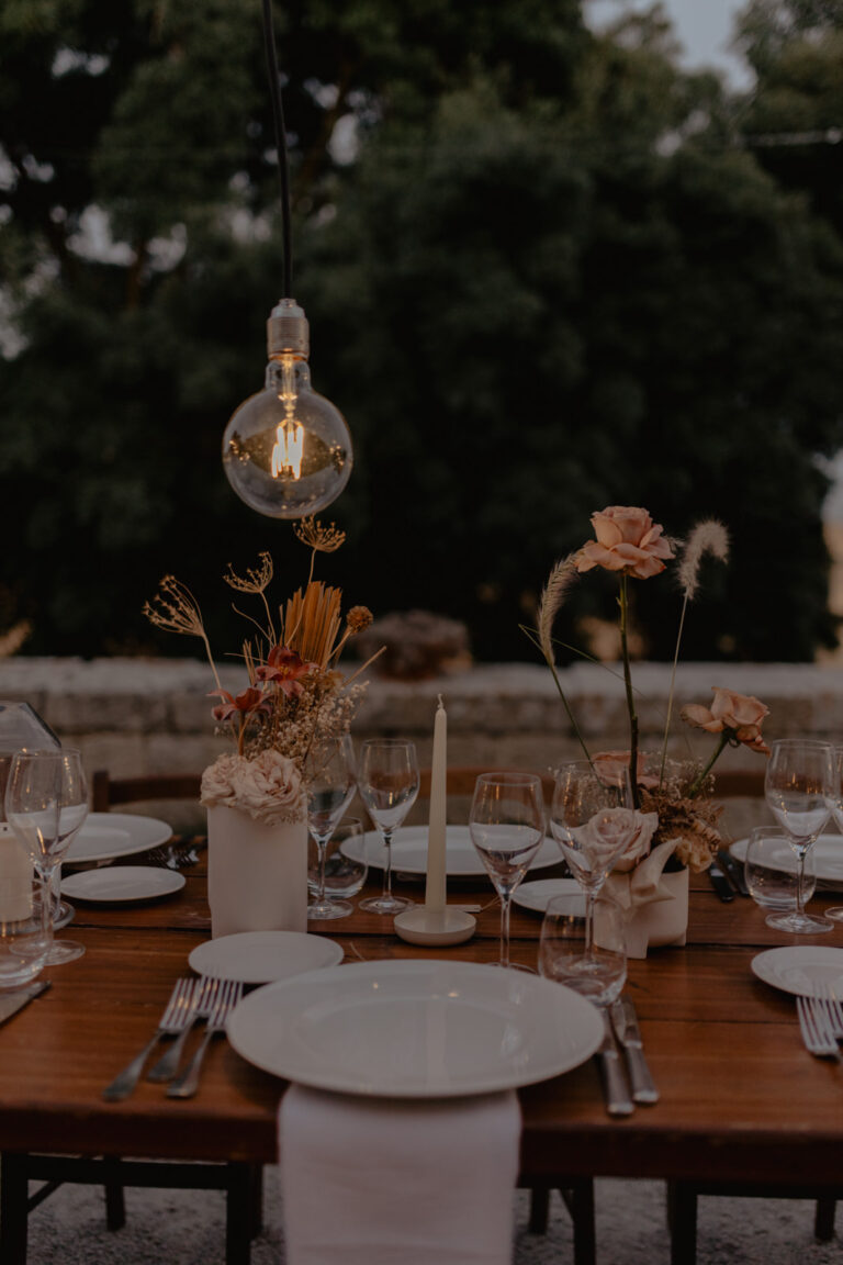 Wooden tables with bud vases, candles and hanging bulbs for dinner at Masseria Susafa, LOVIÙ Events