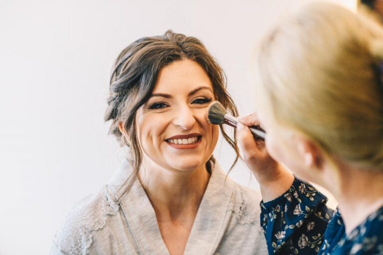 A bride laughing mid-application, blush swept along the cheekbone, Loxus Hair and Makeup