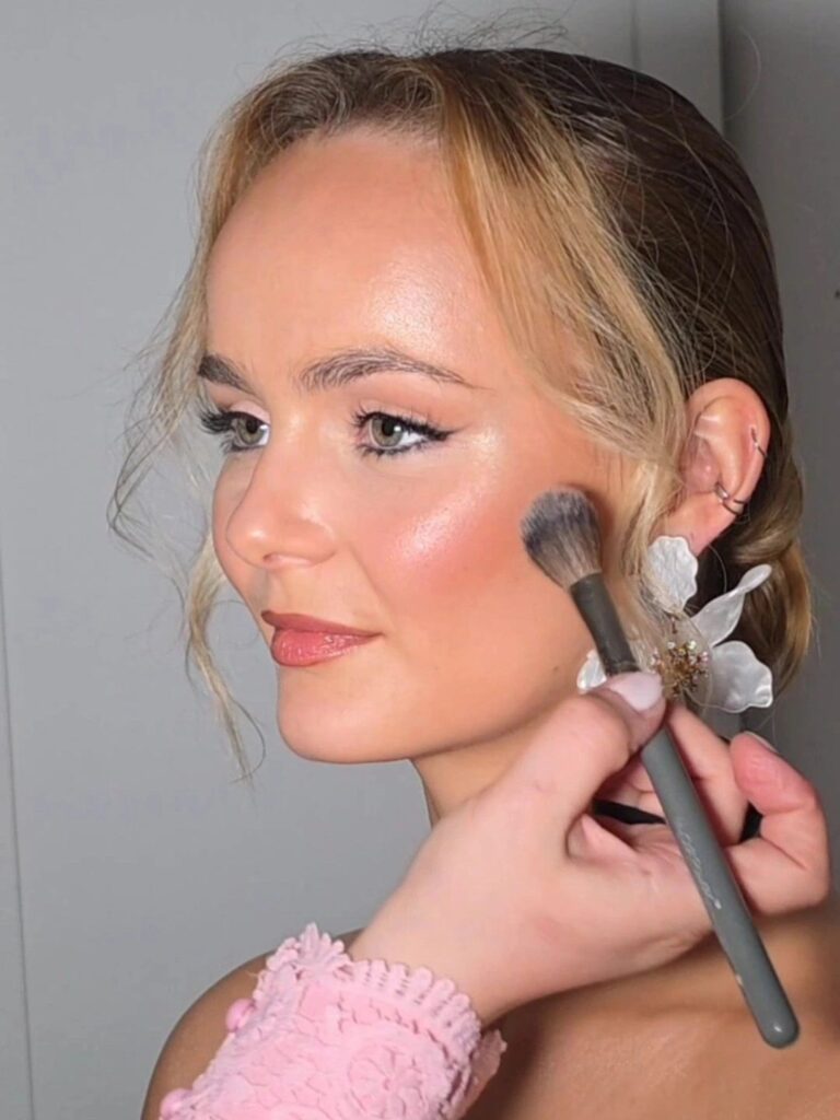 Blush applied to a bride's cheek, a white floral hairpiece, Loxus Hair and Makeup