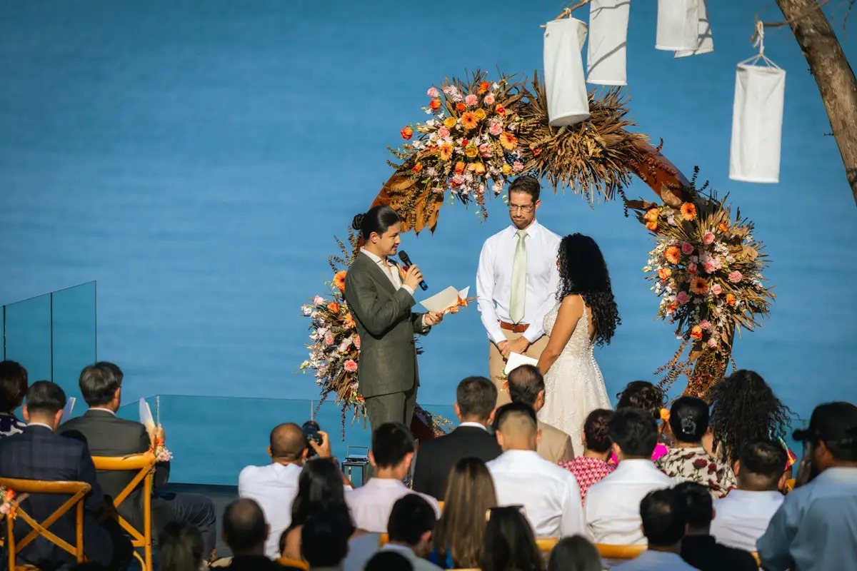 A ceremony under a flower arch and hanging lanterns, with guests seated before a blue sea, Cape Panwa, Phuket, Lucida Image