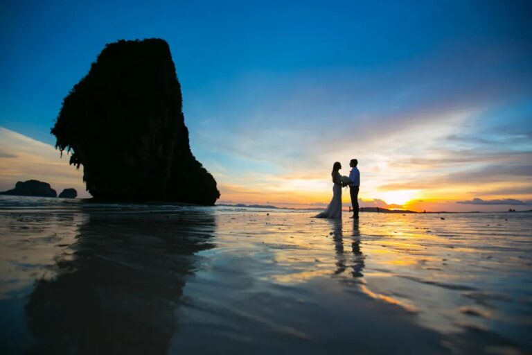 A couple in silhouette against a deep blue and orange sunset beside a limestone rock, Railay, Krabi, Lucida Image